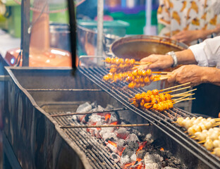 A street food vendor grilling rows of skewered meatballs over hot charcoal at a night market