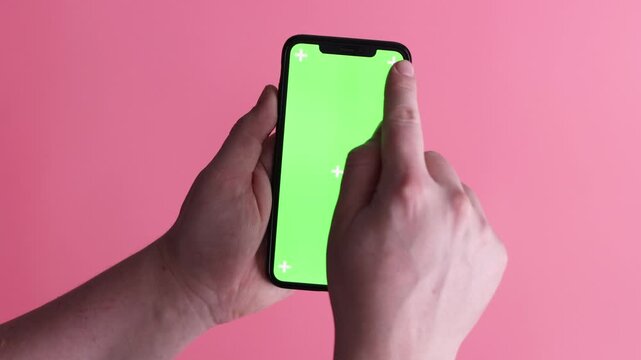 A man's hand holds a phone with a green screen mockup and scrolls through the feed, buys items online, types a message, and closes work tasks on a pink background