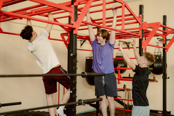 Three friends enjoy a lively workout session at a local gym, taking turns on a red monkey bar setup. Laughter fills the air as they challenge each other in a fun fitness competition.