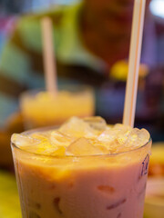 Close up of an iced milk tea in. a plastic cup with a straw with a blur background of a male man.