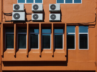 Orange building exterior with rectangle glass window and air conditioning split unit mounted on the wall.