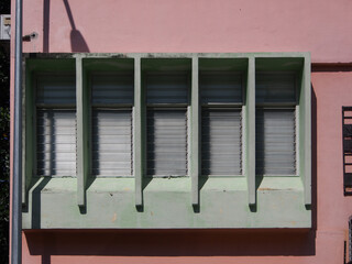 A row of a rectangular louver glass window on a pink painted building exterior with some shadow.
