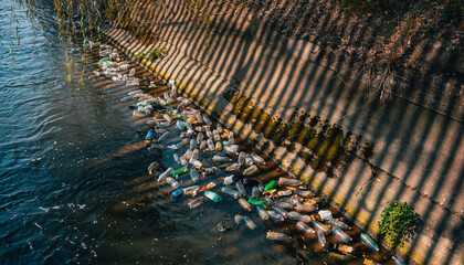 Polluted urban river, floating plastic waste near riverbank, natural daylight with dramatic shadows, environmental education background