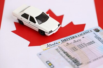 Canadian driving permit concept. Toy car and driver license on flag close up