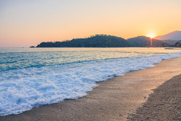 Obraz premium Serene sunset over mediterranean beach with gentle waves and distant hills