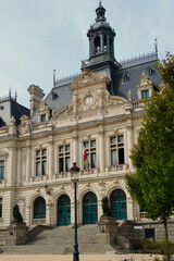 Historic H&ocirc;tel de Ville of Vannes featuring an ornate fa&ccedil;ade, mansard roofs, sculpted stonework, and a prominent central tower, viewed from a foreground garden that enhances its architectural presence