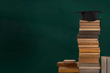 Stacks of books, Square academic cap or graduation hat against the background of a green school board. Concept of education, knowledge, intelligence