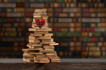 The Love Of Reading. Stacks of books in the shape of a mountain or pyramid against the background of bookshelves. Heart made of fabric. Concept of library, reading, old classic literature