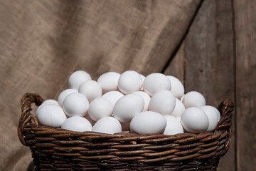 Chicken eggs in large wicker basket with wall of chicken coop, barn or wooden grunge fence in the background. Countryside setting © TSViPhoto