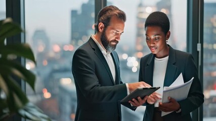 Professional diverse colleagues collaborating in a modern high rise office. A middle aged caucasian manager and young black female employee discuss project strategy on a tablet - Powered by Adobe