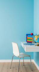 Modern kids study area with white desk and blue wall. Student workspace interior with books, globe and red apple