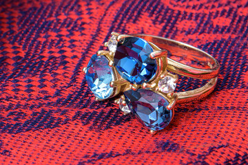 Blue gemstone ring resting on red patterned fabric.