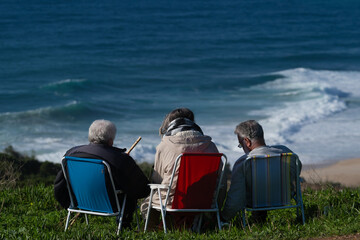 Three people sit in colorful beach chairs facing the ocean, enjoying a peaceful coastal moment