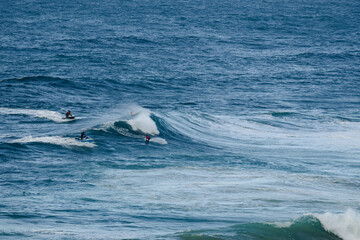 Fototapeta premium Surfers riding large ocean waves, blue water, action and motion on a sunny day at sea