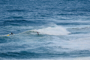 Fototapeta premium Surfers ride a powerful ocean wave as curling white spray crashes nearby