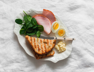 Delicious breakfast, brunch - grilled bread, boiled egg, spinach, ham on a light background, top view