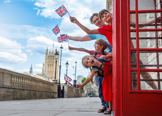 Family of tourists wave UK flags from a phone booth near Big Ben