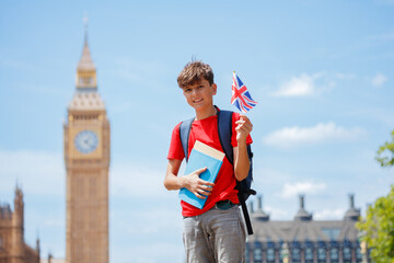Teen boy by Big Ben, clutching notebooks on a sunny London day