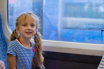 Young girl with pigtails smiles while seated by a train window