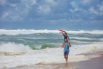 Strolling by the sea, dad and kid on back play small toy plane
