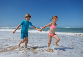 Happy children boy and girl dash through foamy waves at shore
