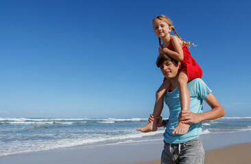 Little girl having fun on her brothers shoulders at the beach