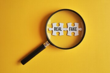 Magnifying glass focusing on real and fake puzzle pieces, for authenticity verification and fact checking, on a yellow background, Business ethics and fraud detection concept with an optical lens.