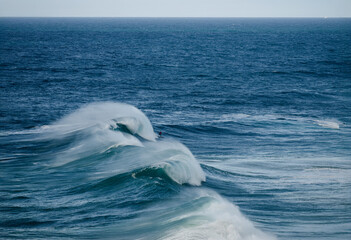 Naklejka premium Powerful ocean waves with surfers riding a breaking barrel under a clear blue sky