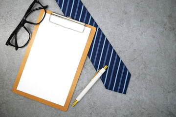 Clipboard with necktie and glasses on stone texture background. Business desk office. Top view
