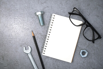 Notebook with glasses and wrench on stone texture background. Business desk office. Top view