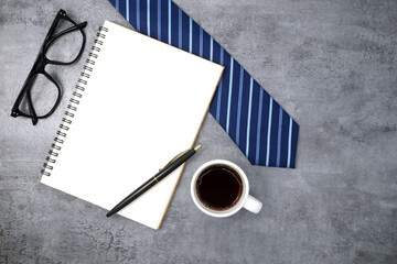 Necktie with notebook and glasses on stone texture background. Business desk office. Top view