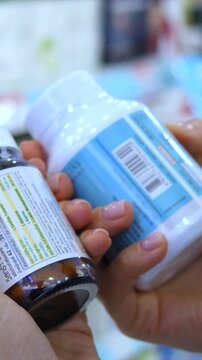 Close up of a customer's hands holding two different bottles of pills, carefully reading the labels and comparing the ingredients and instructions before making a choice in a drugstore aisle