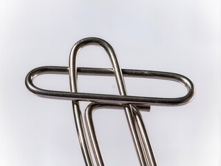 Two paper clips are connected in a simple design on a white background during daylight