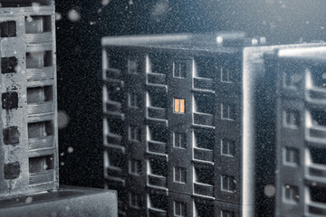 An empty multi-story building with only one window with light at winter snowy night. Abandoned winter city without people concept