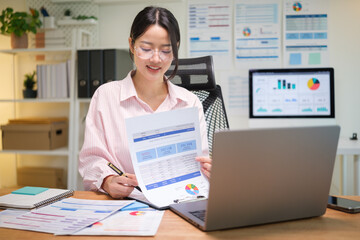 Smiling businesswoman analyzing financial data with printed charts and a laptop in a modern office.