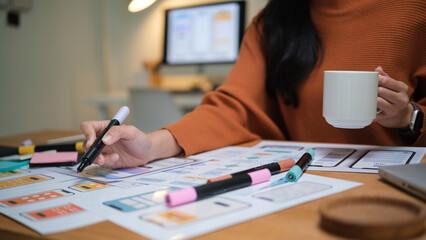 Close-up of UX UI designer’s hands working on wireframes while holding a coffee mug.