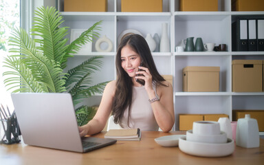 Young woman talking on the phone while working on her laptop at home.