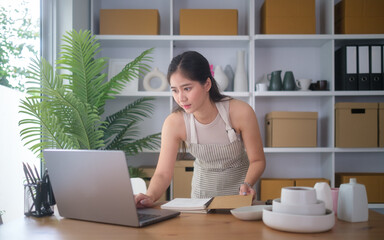 Focused young woman using laptop and notebook in a home workspace.