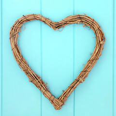 Natural romantic heart shape wicker wreath. Rustic decoration on wooden turquoise background. Symbol of love.