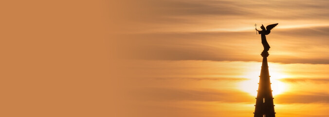 Silhouette of angel statue on cathedral at sunset, concept for religious theme or spiritual meditation for holiday. Banner with copy space