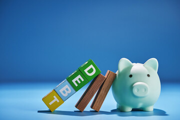 piggy bank and toy block with word debt against blue background