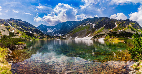Stunning view of Nizne Temnosmrecinske pleso, a glacial lake in the High Tatras National Park, Slovakia. The image features transparent water with rocks on the bottom, surrounding jagged mountain peak