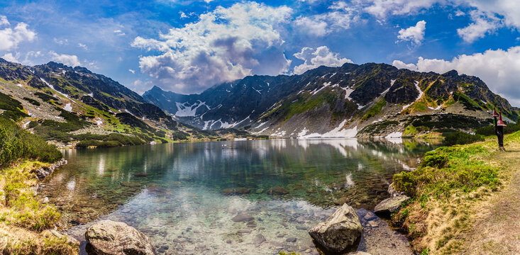 Stunning view of Nizne Temnosmrecinske pleso, a glacial lake in the High Tatras National Park, Slovakia. The image features transparent water with rocks on the bottom, surrounding jagged mountain peak