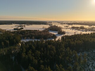 Fototapeta premium Aerial view of winter forest and snow-covered countryside at golden hour