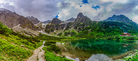 A dramatic landscape shot of a hiking path at the edge of Green Lake (Zelene pleso). Massive granite peaks with snow patches are shrouded in heavy grey storm clouds. Tatra National Park, Slovakia. © Ivan