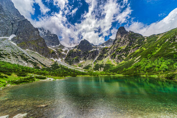 A breathtaking wide panorama of Zelene pleso (Green Lake) in the High Tatras, Slovakia. The image features the iconic mountain hut, crystal clear water with a rocky bottom, and jagged granite peaks un