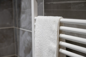 White towel hanging on a towel rack in a modern bathroom with gray tiles and a simple design