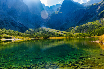 A stunning view of the crystal clear Green Lake (Zelene pleso) showing the rocky lakebed. Surrounded by massive granite walls and peaks under bright sunlight in the Tatra National Park.