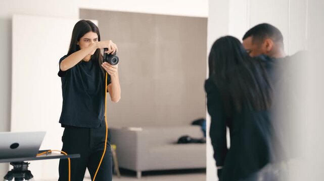 Photographer taking photos of a couple in a professional studio, using a digital camera connected to a laptop - Powered by Adobe
