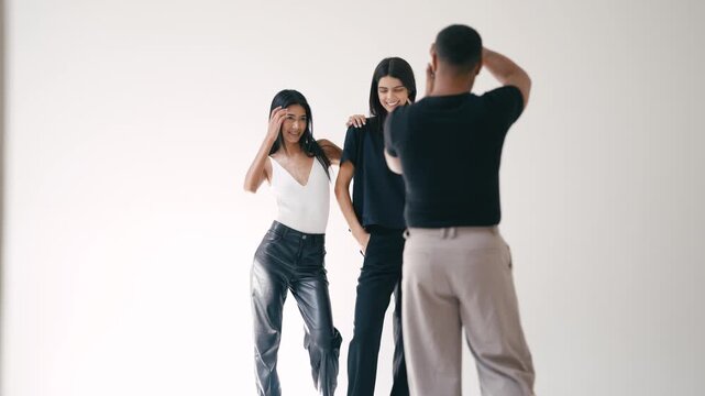 Photographer taking photos of two female models posing on white background in professional studio